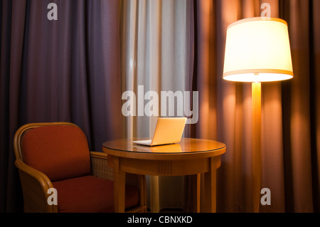 notebook computer on the table in the room with lamp, chair and curtains on the window Stock Photo