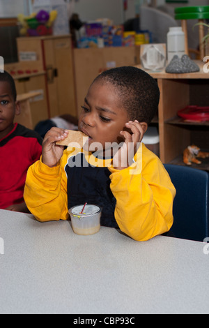 4 year old African American preschool boy drinking apple juice and eating crackers during snack time Stock Photo