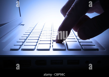 Man hand and laptop keyboard. Blue toned image. Backlit scene. Stock Photo