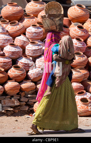 Indian woman out shopping carrying child walks past clay water pots on sale in old town Udaipur, Rajasthan, Western India, Stock Photo