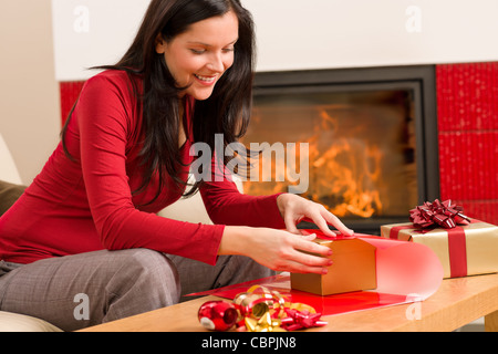 Happy woman in red wrapping Christmas present by home fireplace Stock Photo