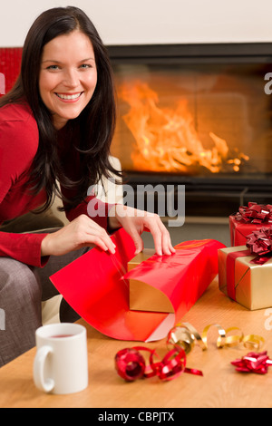 Happy woman in red wrapping Christmas present by home fireplace Stock Photo