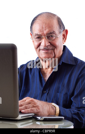 Portrait of a smiling elderly East Indian businessman on his computer laptop Stock Photo