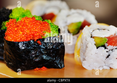 Plate of assorted sushi rolls with focus on front rolls including a colorful fish roe topped roll. Stock Photo