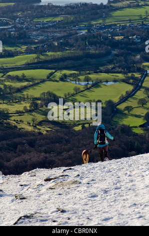 A walker and her dog coming down a snowy Skiddaw in Cumbria, England, UK Stock Photo