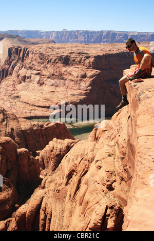 a man sits on the edge of a sandstone cliff overlooking Glen Canyon, Arizona Stock Photo