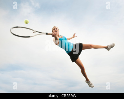 Caucasian woman jumping in mid-air playing tennis Stock Photo