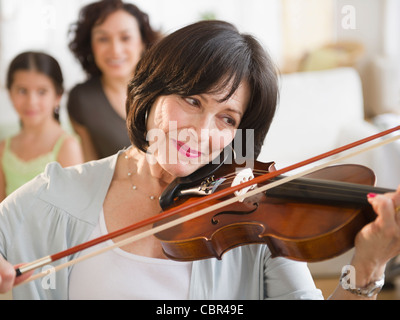 Mother and daughter watching grandmother playing violin Stock Photo