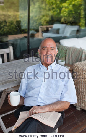 https://l450v.alamy.com/450v/cbr93e/man-sitting-on-patio-drinking-coffee-and-reading-newspaper-cbr93e.jpg