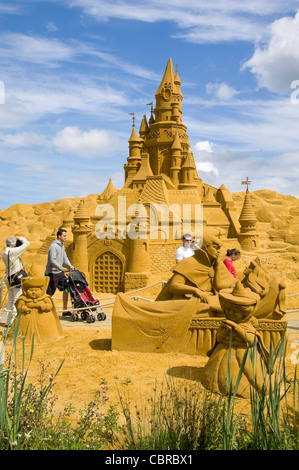 Vertical close up of an amazing sand sculpture of a huge castle with people walking passed to give it scale, on a beautiful day. Stock Photo