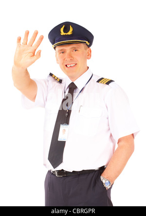 Cheerful airline pilot wearing uniform with epaulettes and hat waving, standing isolated on white background. Stock Photo