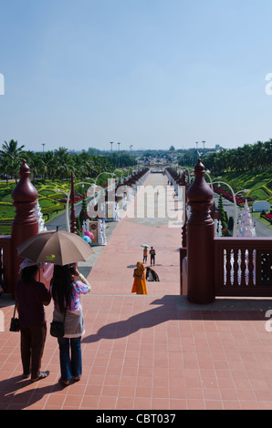 Two women standing with an umbrella for shade in front of long pedestrian promenade & Buddhist monk in orange robe on staircase Stock Photo