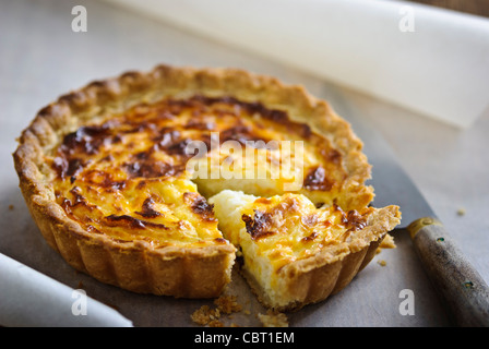 Little Quiche Lorraine (cheese and onion tart) on curled greaseproof paper with knife Stock Photo