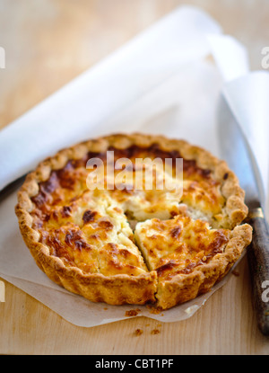 Little Quiche Lorraine (cheese and onion tart) on curled greaseproof paper with knife Stock Photo