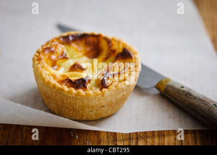 Little Quiche Lorraine on curled greaseproof paper with knife Stock Photo