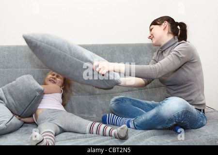 Little child and young mother in pillow fighting on the sofa. Funny and happy leisure. Stock Photo