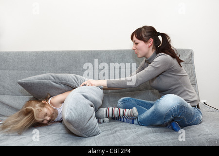 Little child and young mother in pillow fighting on the sofa. Funny and happy leisure. Stock Photo