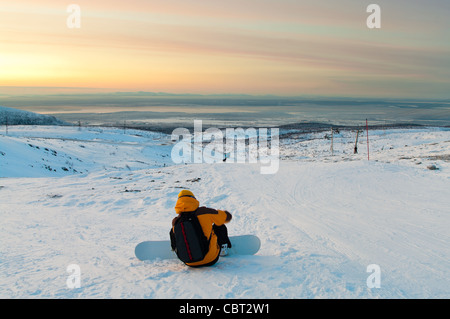 Snowboarder sitting on the mountain slope and looking through the distance. Khibins mountains in Kola peninsula. Polar night Stock Photo