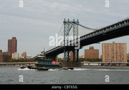 Tugboat moving on grey waters East River, south of Manhattan Bridge mid-span,  towards Manhattan from Brooklyn Fulton Ferry Park Stock Photo