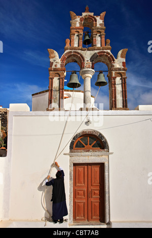 A Greek Orthodox priest ready to toll the bells of a church in picturesque Pyrgos village, Santorini island, Cyclades, Greece Stock Photo