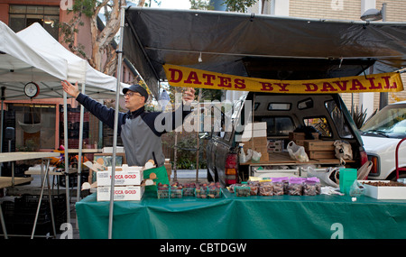 A man selling dates at a farmer's market in California gestures to a friend. Stock Photo