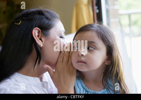 Hispanic mother whispering to daughter Stock Photo