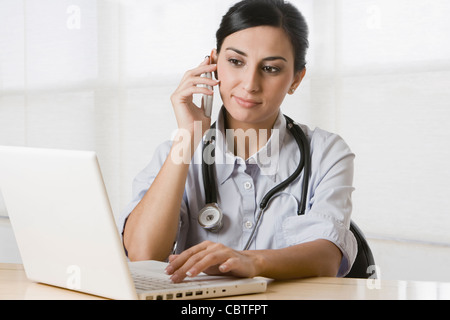 Turkish doctor talking on cell phone and using laptop Stock Photo