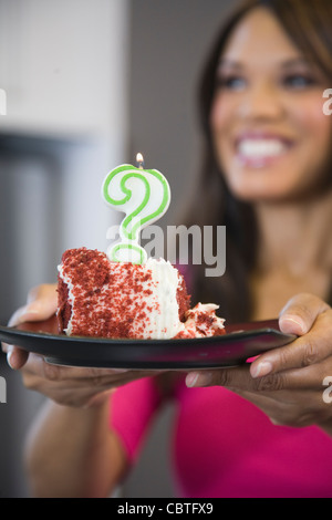 Mixed race woman holding cake with question mark candle Stock Photo