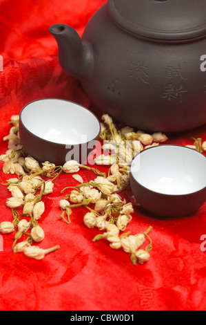 jasmine tea dry flowers,pot and two cups ,over red silk tablecloth Stock Photo