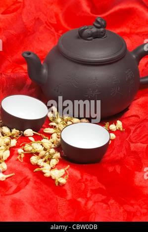 jasmine tea dry flowers,pot and two cups ,over red silk tablecloth Stock Photo