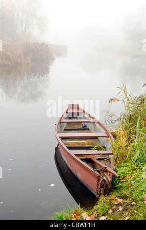 Wooden rowing boat stands on coast of river sunken in dense fog. Stock Photo