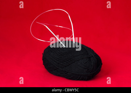 Ball of yarn and knitting skewers. Black yarn on red background Stock Photo