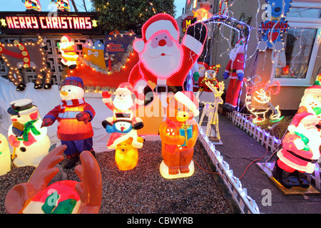 Glowing illuminated gaudy plastic kitsch Christmas decorations in garden of suburban semi-detached UK house, Suffolk, England Stock Photo