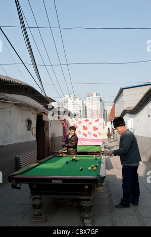 Xiadian, Beijing. Men playing pool in a poor neighborhood with in the background Beijing's Central Business District. Stock Photo