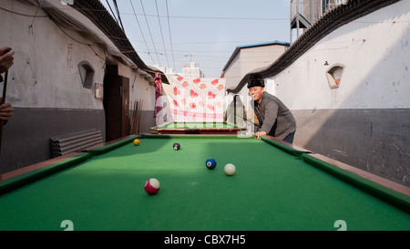 Xiadian, Beijing. Man playing pool in a poor neighborhood with in the background Beijing's Central Business District. Stock Photo