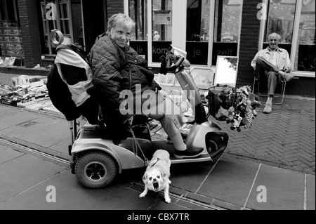 Enschede, The Netherlands. Woman in a mobility scooter with dog. In the background a jumble sale on the street. Stock Photo