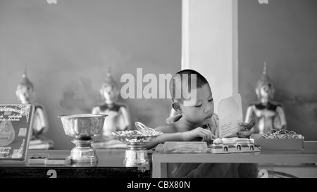 Wat Yai Suwannaram Temple, Petchaburi, Thailand. Young monk reading in the temple. Stock Photo