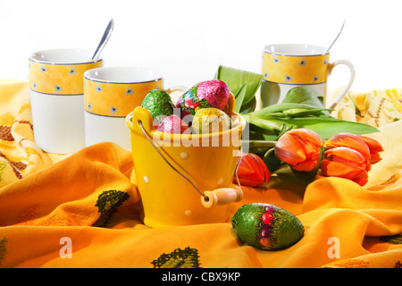 Easter decoration - small bucket with chocolate eggs, table-cloth and mugs Stock Photo