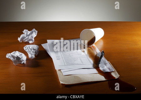 Crumpled paper spilled coffee and tax form on desk Stock Photo