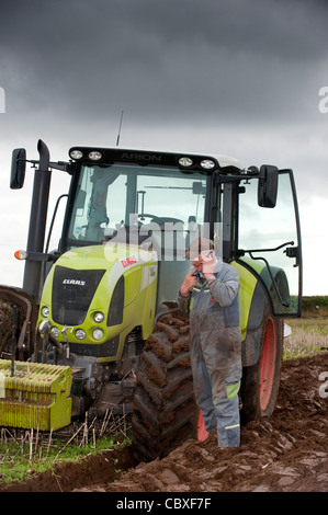 Farmer talking on mobile phone whilst standing in front of stationary tractor. Stock Photo