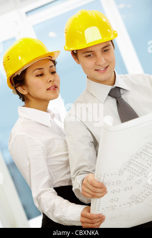 Portrait of two architects in helmets looking at document at meeting Stock Photo