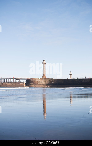 A view of a lighthouse on Whitby Pier with reflection in Whitby Beach, on a bright Spring day. Whitby, North Yorkshire, UK. Stock Photo