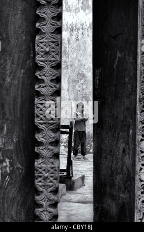 View of a young African boy through a doorway standing poised with his hands crossed in a courtyard in Stone Town, Zanzibar Stock Photo