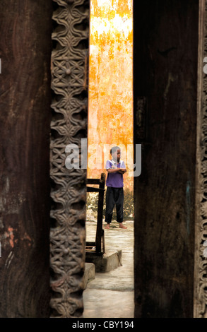 View of a young African boy through a doorway standing poised with his hands crossed in a courtyard in Stone Town, Zanzibar Stock Photo