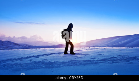 Woman traveler hiking in winter mountains, trekking in wintertime cold snowy weather, girl silhouette over natural blue sky Stock Photo