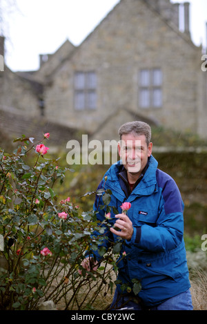 Media Photo Call - Chris Clennet the garden manager at Wakehurst Place in Sussex with an Eve Price rose which is still in bloom in December Stock Photo