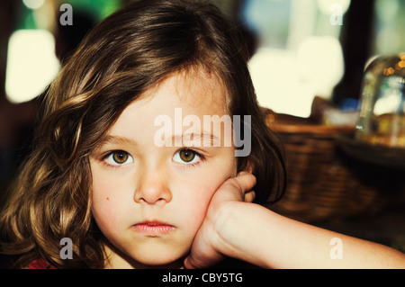 Cute portrait of a young 5 year old brunette girl pouting with big brown eyes gazing into the camera. Amyn Nasser Stock Photo