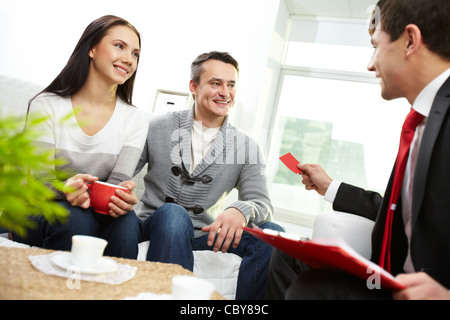 Portrait of modern couple looking at real estate agent giving his visiting card Stock Photo