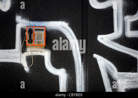 Orange public telephone on a graffiti wall Stock Photo