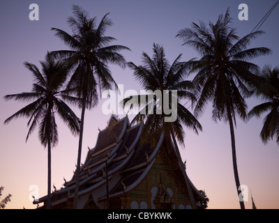 Tropical coconut palms grace Haw Pha Bang (Golden Hall) at sunset in Luang Prabang, Laos. Stock Photo